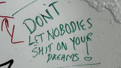 Some graffiti on a white wall, it says “Don’t let nobodies shit on your dreams!” The exclamation mark uses a heart instead of a dot.