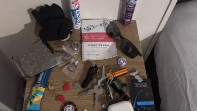 A bedside table with the contents of my pockets from the last week or so:

- Several stickers
- Some coin cell batteries
- Two red and one gold tiny plastic rabbit
- Key ring
- A small pile of EMF meal tokens
- AirPods
- Sunglasses
- EMF 2026 pins
- A USB cable
- Two Unaffiliated Village tokens featuring Tim Curry shouting SPAAAACE
- An EMF info booklet
- Keebdeck
- Some work gloves
- Three tubes of hydrating salts
- A volunteer team lead badge with my name on it
- A button style badge with an alien on it saying “Excellent Work”