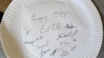 A paper plate reading Happy EMF 2026 and signed by several people.